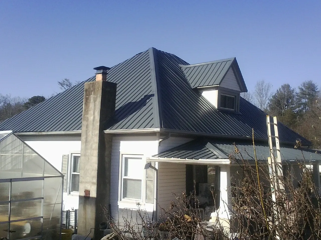 Dark blue standing seam metal roof on a white farmhouse with dormer — Slate & Tile Roof Repair by Roofing Brothers in Lone Jack