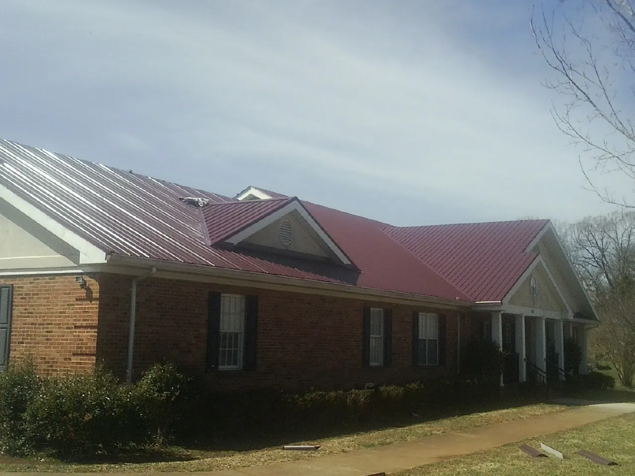 Red metal roof with gabled entries on a long brick building, from a Hail Damage Roof Repair job in Lone Jack