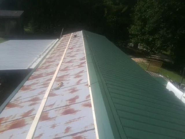 Old rusted panels beside newly installed green metal roofing — Wind Damage Roof Repair by Roofing Brothers in Lone Jack