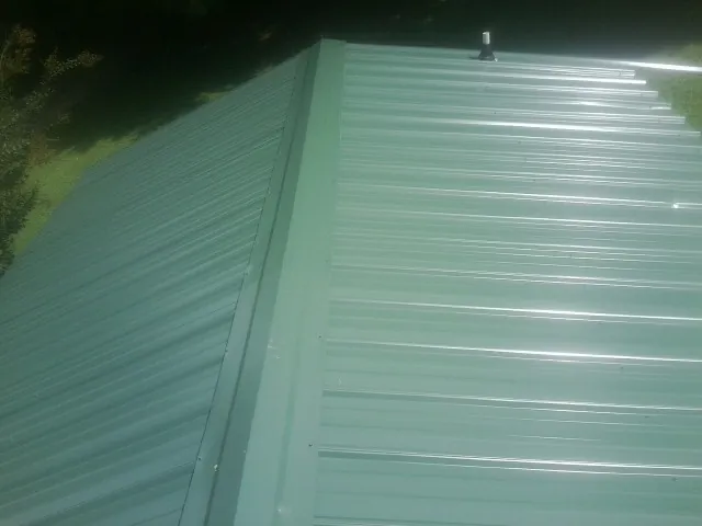 New green metal panels meeting at the ridge of a roof — Flat Roof Repair work by our crew in Lone Jack
