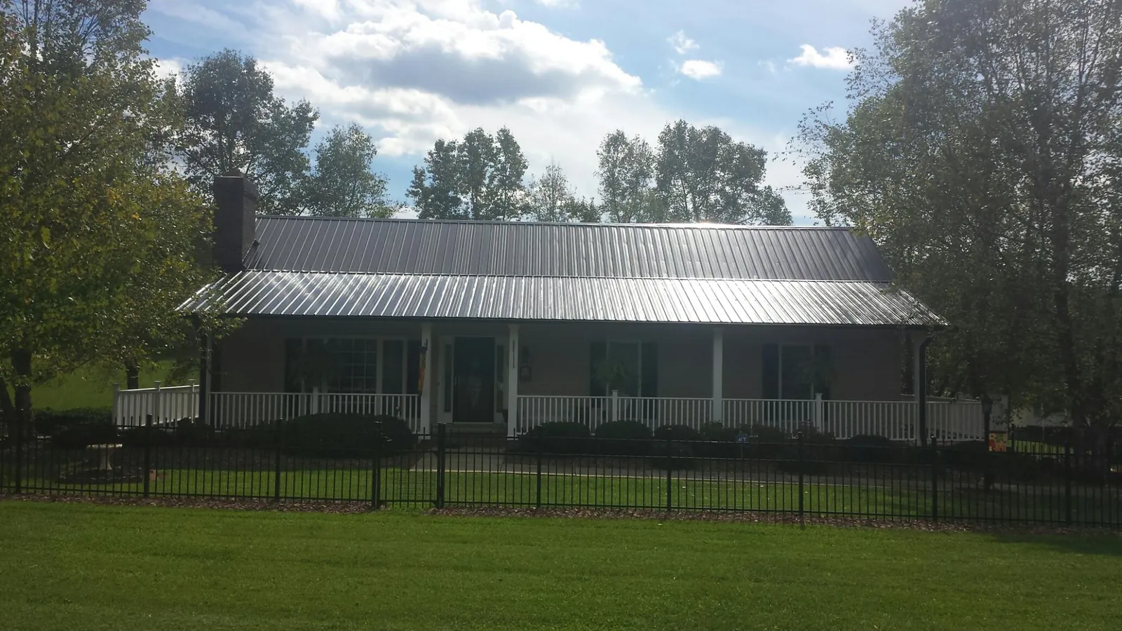 Gray metal roof on a brick ranch with a full width front porch — Gutter Guard Installation work by our crew in Lone Jack