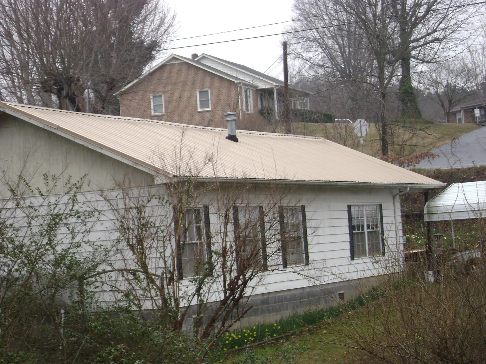 Tan metal roof on a white sided house set into a hillside — Commercial Roofing by Roofing Brothers in Lone Jack