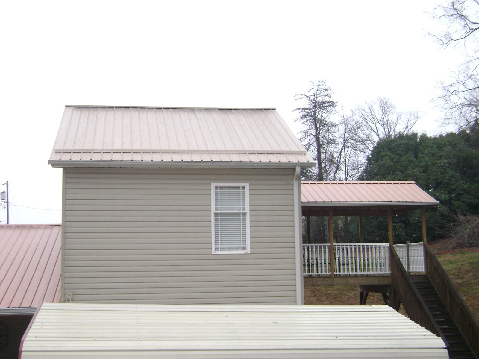Tan metal roofs on a two story addition and attached porch, from a Roof Replacement job in Lone Jack